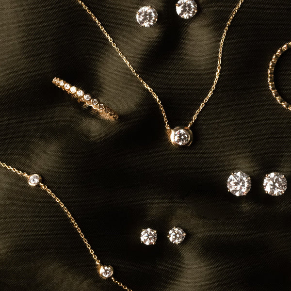 Mulitple pieces of gold jewelry with clear gemstones and clear diamonds, laying on a dark green satin surface.