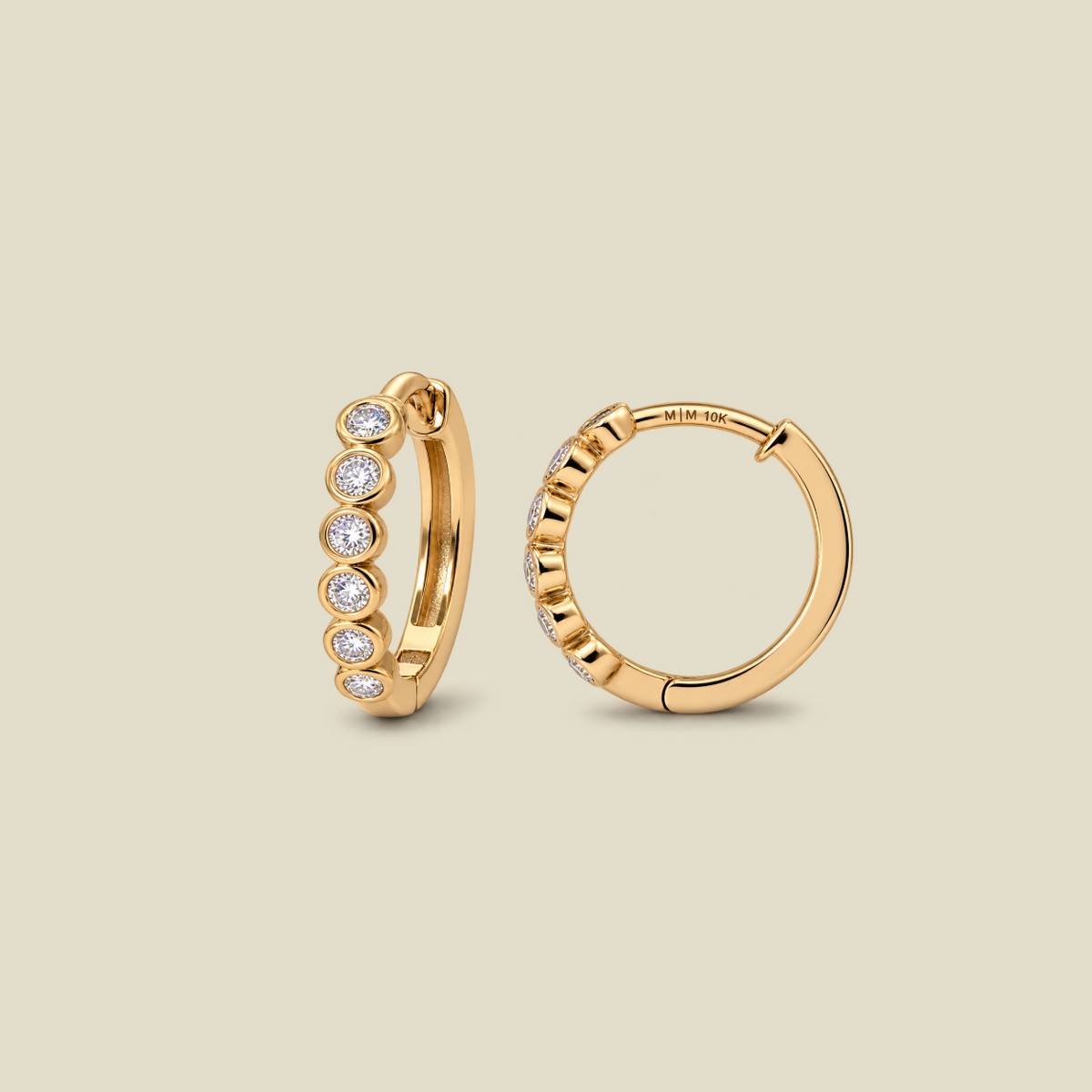A pair of gold huggie hoop earrings, one shown from the front with six bezel-set round clear diamonds and the other from the side showing the hinge closure. The earrings are displayed on a solid light beige background.
