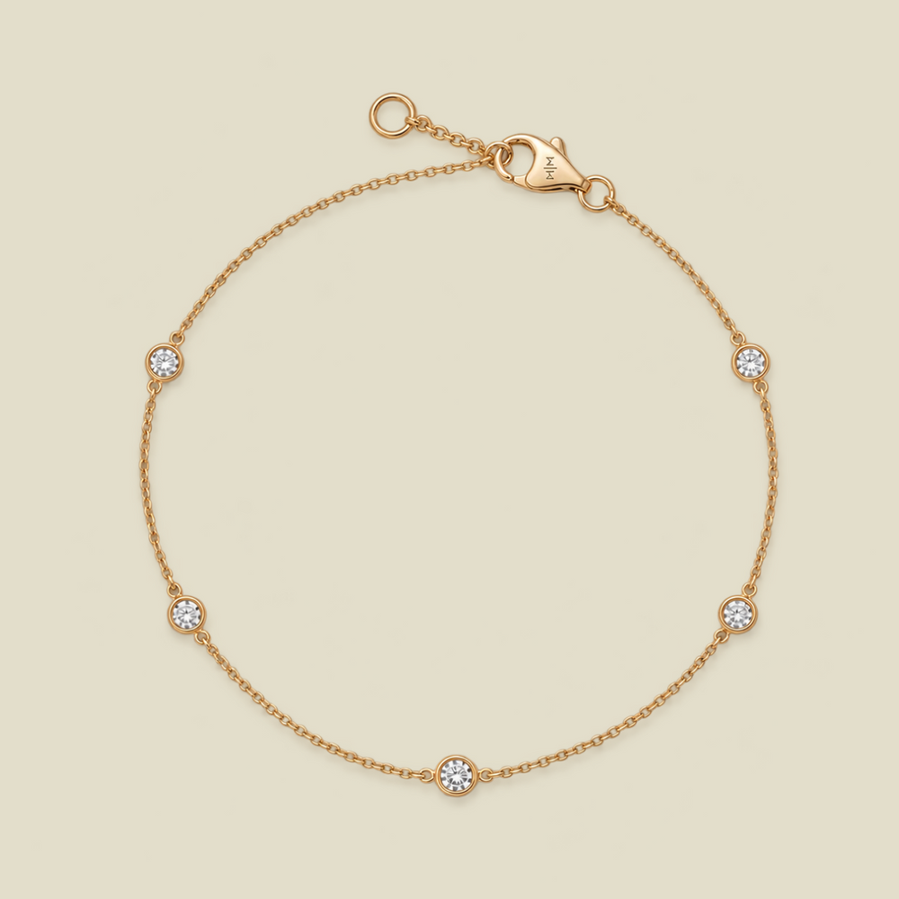 A delicate gold chain bracelet with five small round bezel-set diamonds spaced evenly along the band, shown on a light beige background.