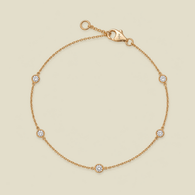 A delicate gold chain bracelet with five small round bezel-set diamonds spaced evenly along the band, shown on a light beige background.