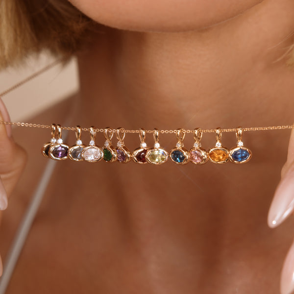 A close-up lifestyle shot of a model holding a delicate gold chain necklace with multiple small, colorful gemstone charms dangling horizontally across her neck.