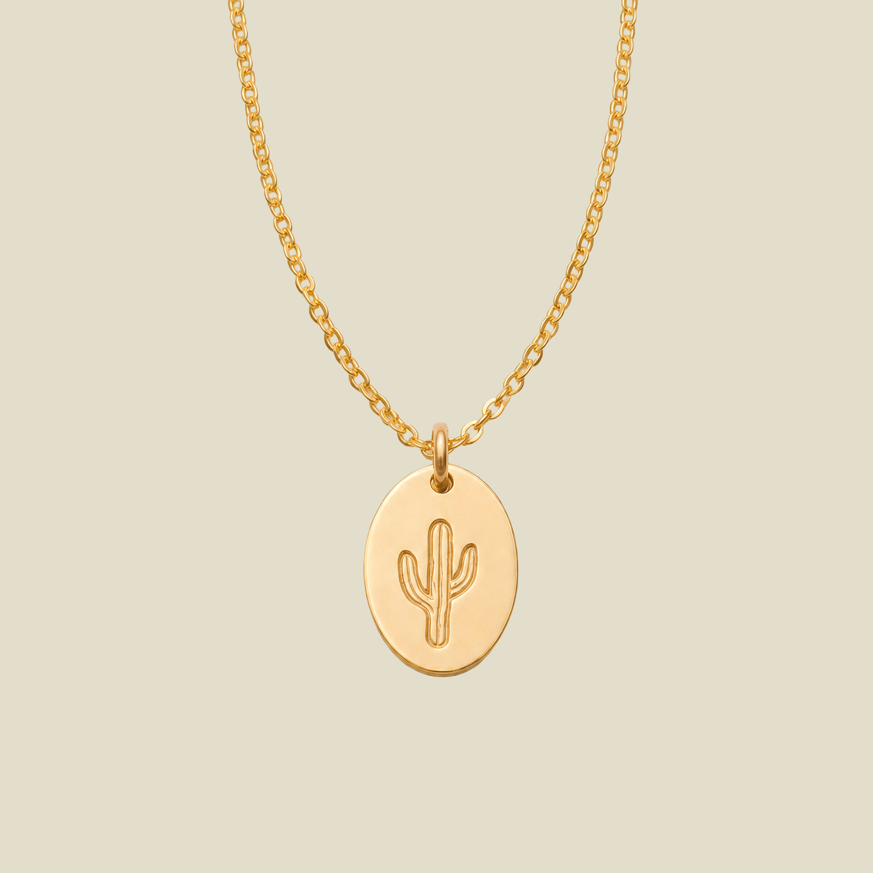 A gold chain necklace with an oval gold pendant featuring an embossed cactus design, displayed against a solid light beige background.