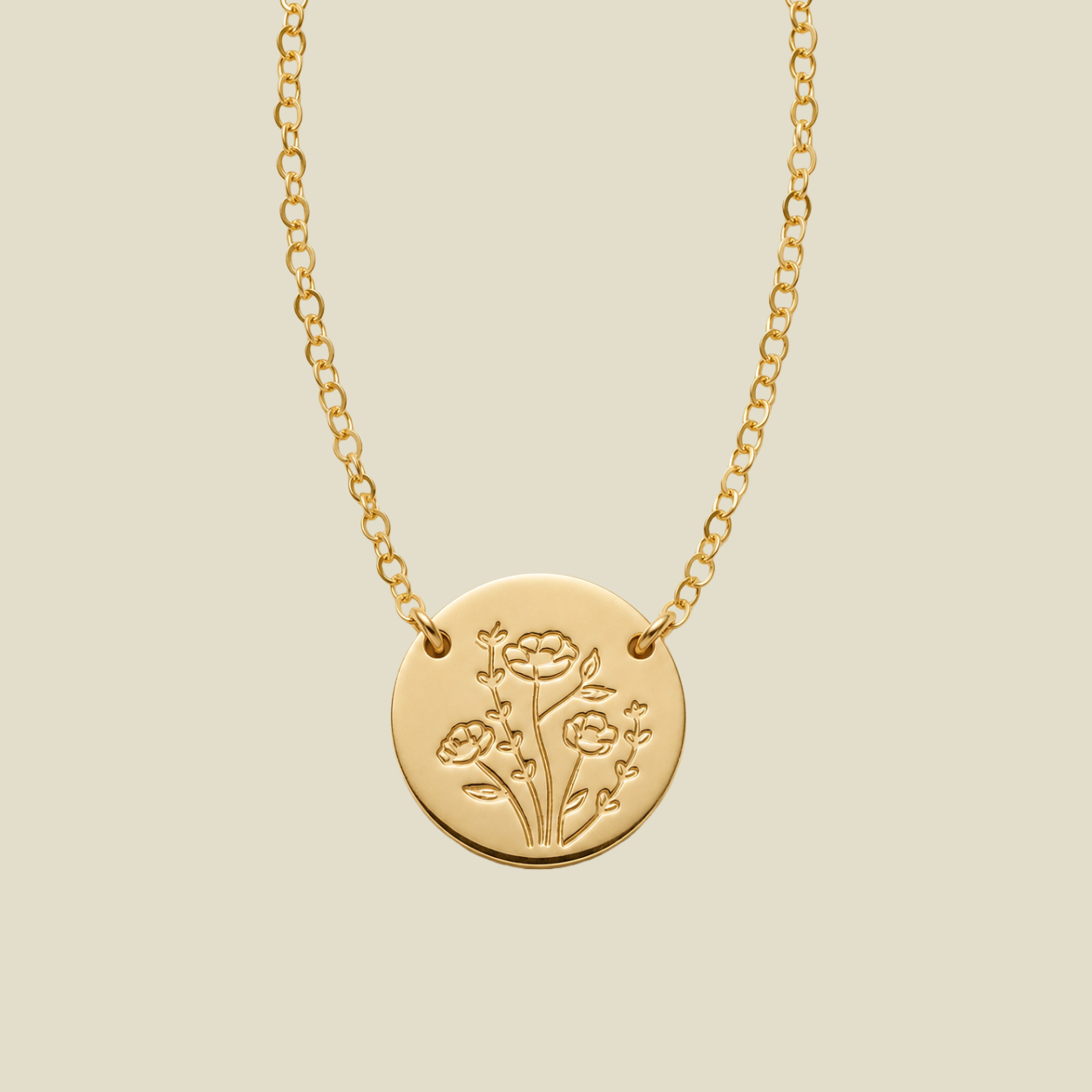 A gold chain necklace with a round gold disc pendant, attached to the chain at two points on the upper part of the disc, engraved with a floral design, shown against a solid light beige background.