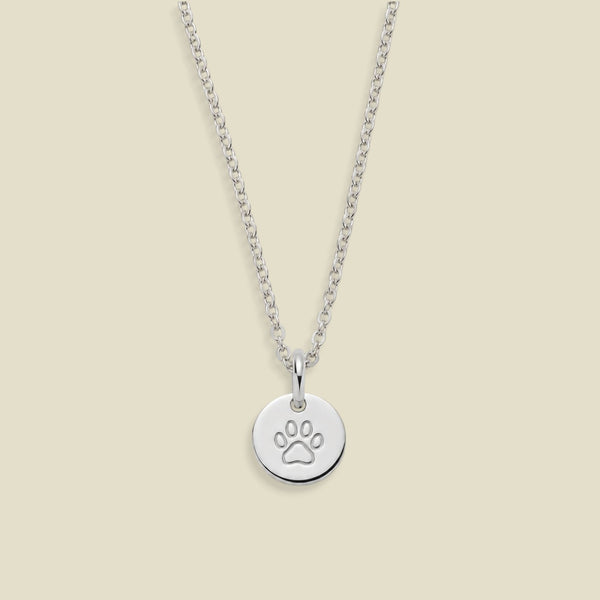 A silver chain necklace with a round disc pendant engraved with a paw print, displayed against a solid light beige background.