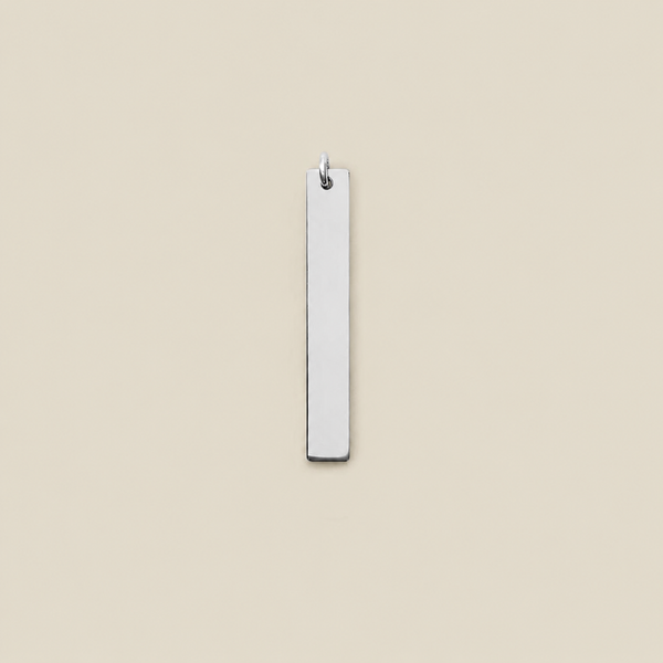 A minimalist, polished silver rectangular bar pendant with a small hanging loop at the top, shown against a solid, warm beige background.