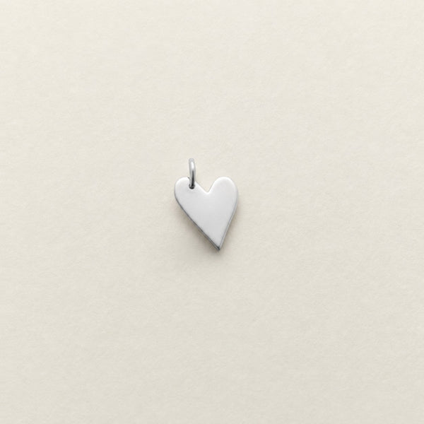 A small, polished silver heart-shaped pendant with a top loop, centered on a textured off-white background.
