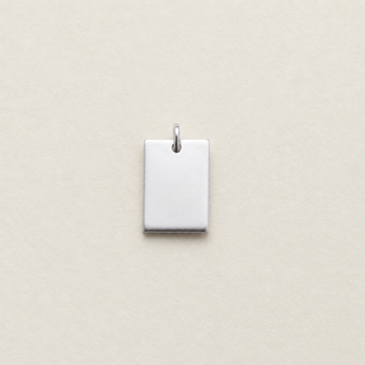 A small rectangular silver pendant with a top loop, shown centered on a light beige textured background.