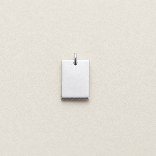 A small rectangular silver pendant with a top loop, shown centered on a light beige textured background.
