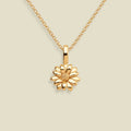 A gold daisy pendant necklace on a delicate gold chain, set against a solid light beige background.