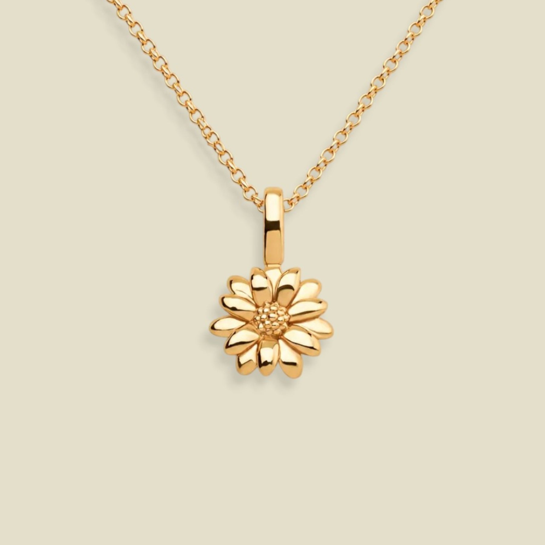 A gold daisy pendant necklace on a delicate gold chain, set against a solid light beige background.