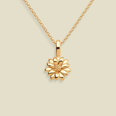 A gold daisy pendant necklace on a delicate gold chain, set against a solid light beige background.