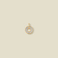 A circular gold pendant featuring clear baguette-cut stones around a hollow center, displayed against a solid light beige background.