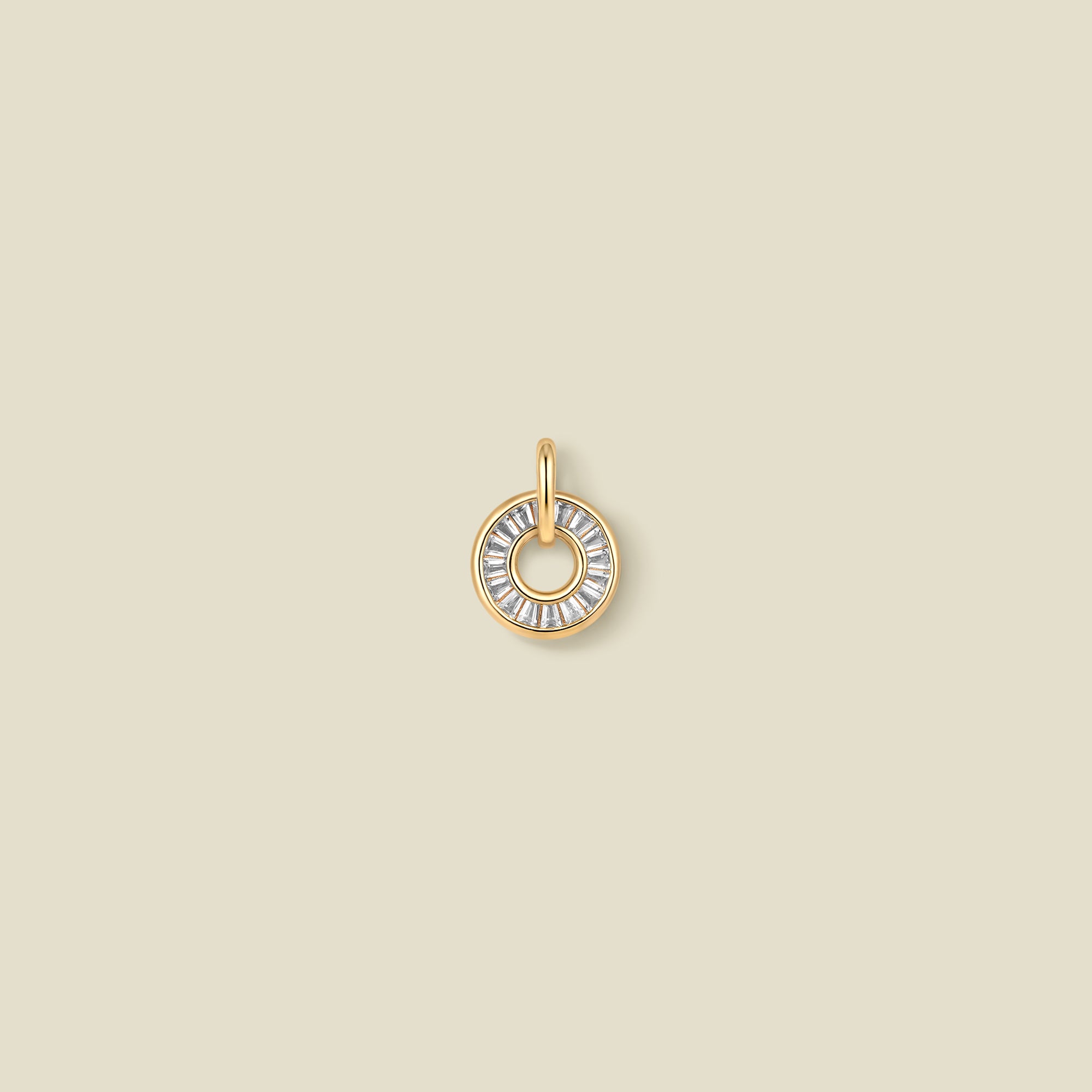 A circular gold pendant featuring clear baguette-cut stones around a hollow center, displayed against a solid light beige background.