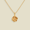 A gold chain necklace with a small, detailed poppy flower pendant, shown against a solid light beige background.