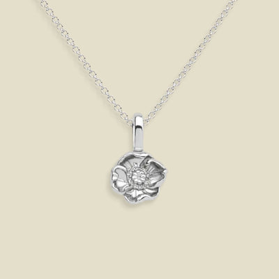A silver poppy flower pendant necklace with a delicate chain, displayed against a solid beige background.