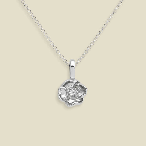 A silver poppy flower pendant necklace with a delicate chain, displayed against a solid beige background.