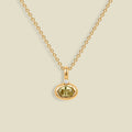 A delicate gold chain necklace with a small oval pendant featuring a faceted olive-green gemstone and a tiny clear accent stone above it, displayed on a solid light beige background.