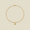 A delicate gold wire necklace with a small oval pendant featuring a green gemstone, displayed on a solid light beige background.
