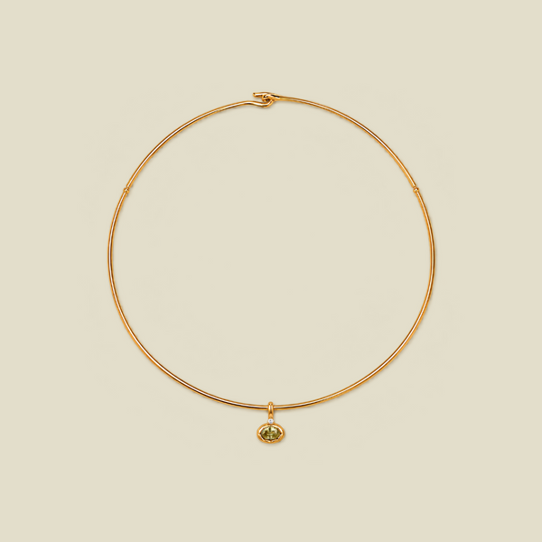 A delicate gold wire necklace with a small oval pendant featuring a green gemstone, displayed on a solid light beige background.