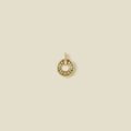 A circular gold pendant featuring light green baguette-cut stones around a hollow center, displayed against a solid light beige background.