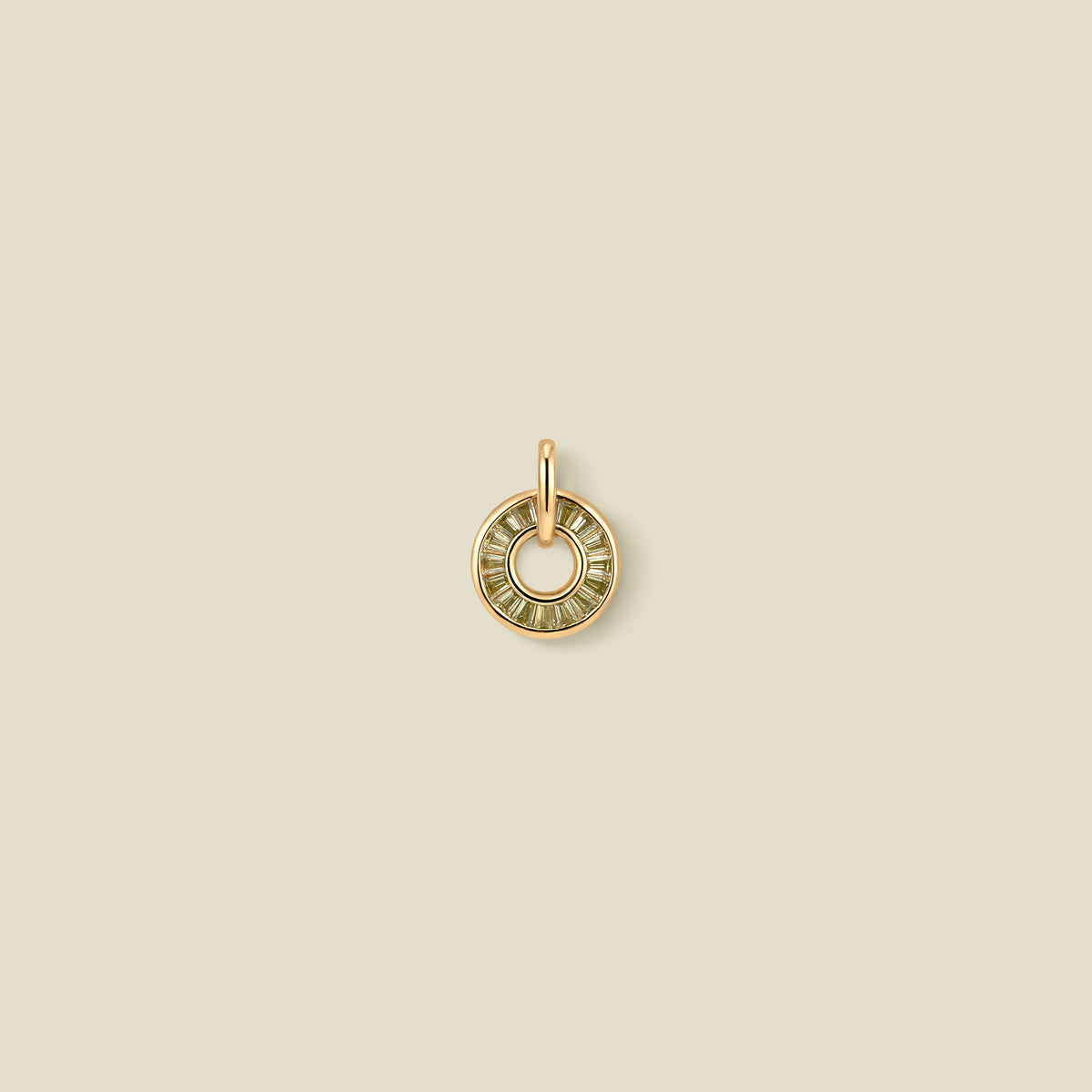 A circular gold pendant featuring light green baguette-cut stones around a hollow center, displayed against a solid light beige background.
