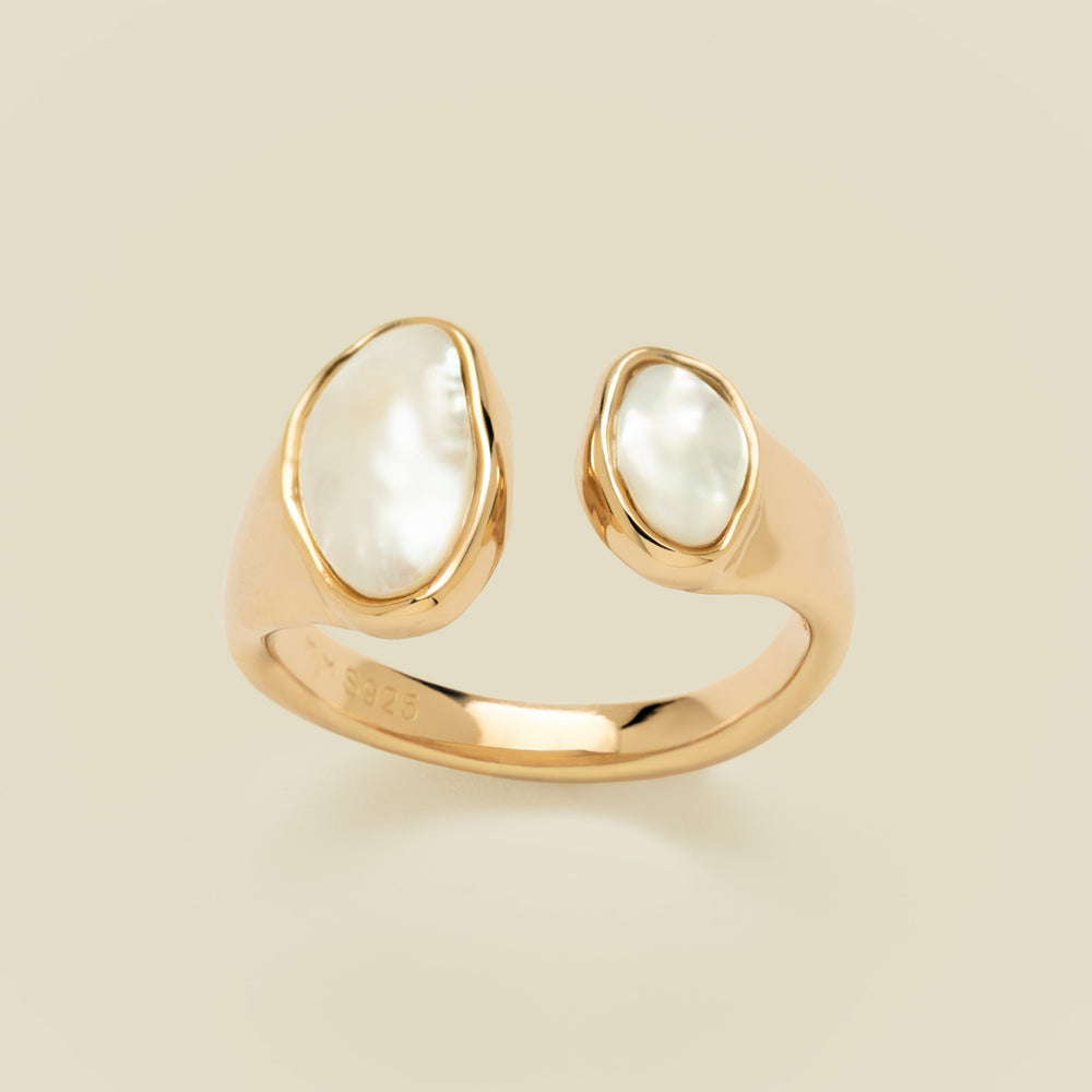 Open ring with two bezel-set pearls against a plain beige background.