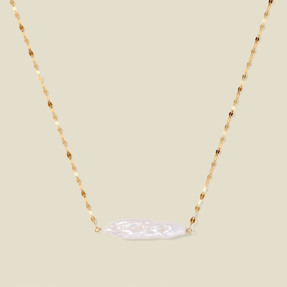 Gold lace chain with a baroque pearl pendant, suspended against a neutral background.