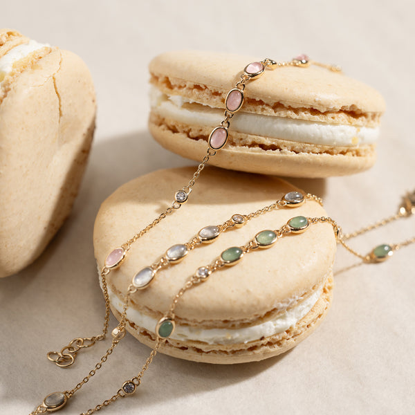 A pink, white and green bezel-set stone bracelets laying on top of two macaron cookies. 