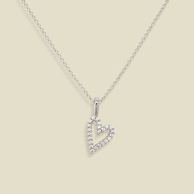 A silver heart-shaped pendant necklace adorned with small clear stones, suspended from a delicate silver chain against a solid beige background.