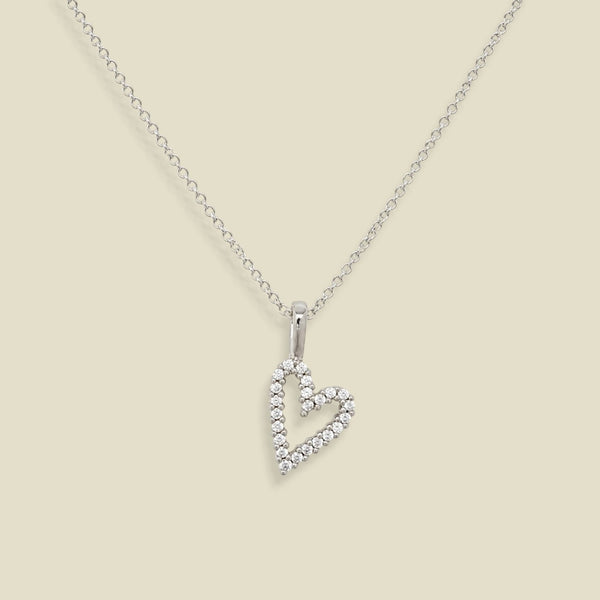 A silver heart-shaped pendant necklace adorned with small clear stones, suspended from a delicate silver chain against a solid beige background.