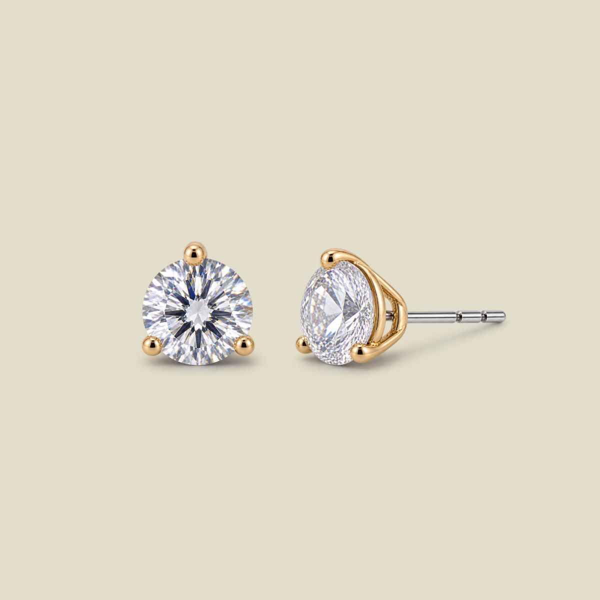 Two stud earrings on a warm beige background, one showing the front view of a round brilliant-cut clear gemstone in a gold prong setting, and the other showing the side profile with a silver-toned post and gold-toned end.