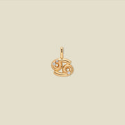 A gold pendant shaped like the Cancer zodiac symbol, featuring three small clear gemstones, centered on a solid light beige background.