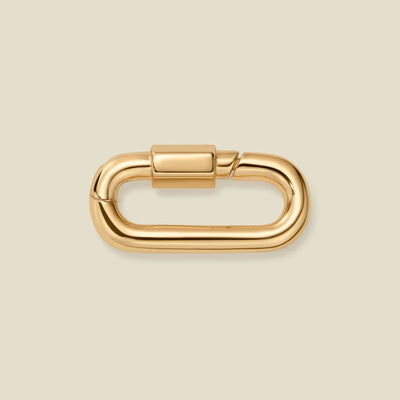 A polished gold metal carabiner clasp with a rounded rectangular shape, shown on a solid light beige background.