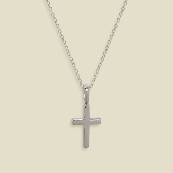 A silver cross pendant necklace on a delicate silver chain, displayed against a solid light beige background.