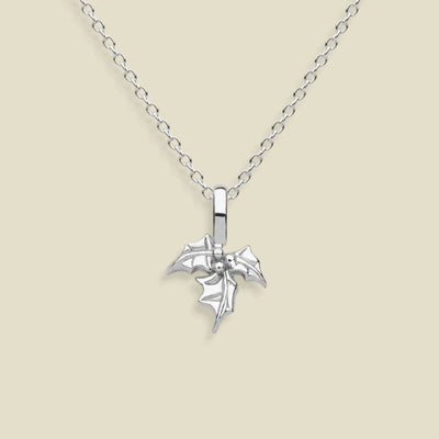 A silver pendant necklace featuring a small, detailed holly flower charm on a delicate link chain, set against a solid light beige background.