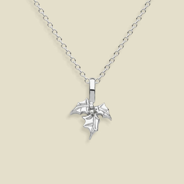 A silver pendant necklace featuring a small, detailed holly flower charm on a delicate link chain, set against a solid light beige background.