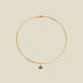 A delicate gold wire hoop necklace with a small oval blue gemstone pendant, displayed on a solid light beige background.