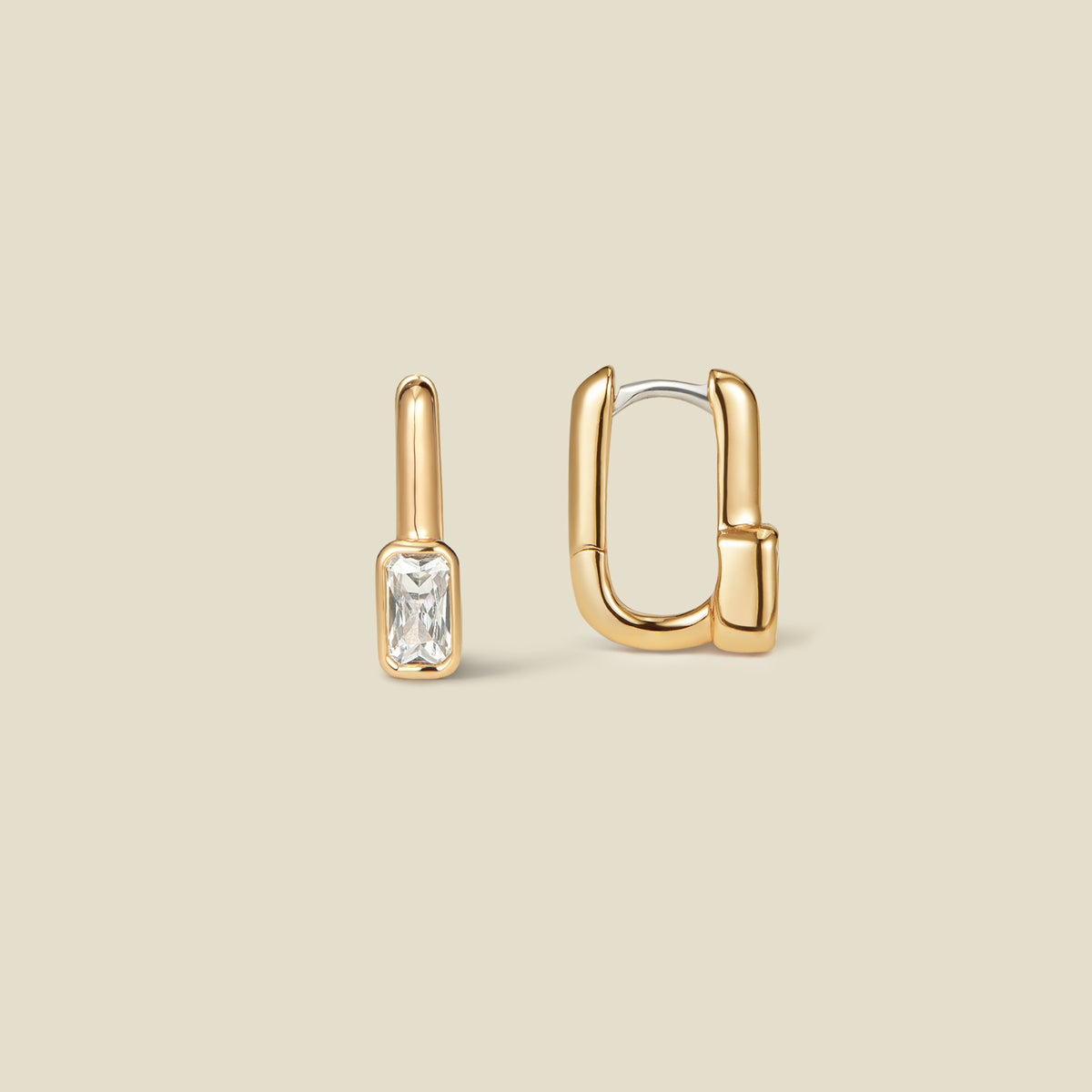 A pair of gold huggie hoop earrings, one shown front-facing with a rectangular bezel-set clear gemstone and the other shown from the side, on a solid beige background.