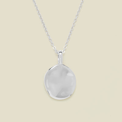 Silver necklace with a round pendant on a beige background