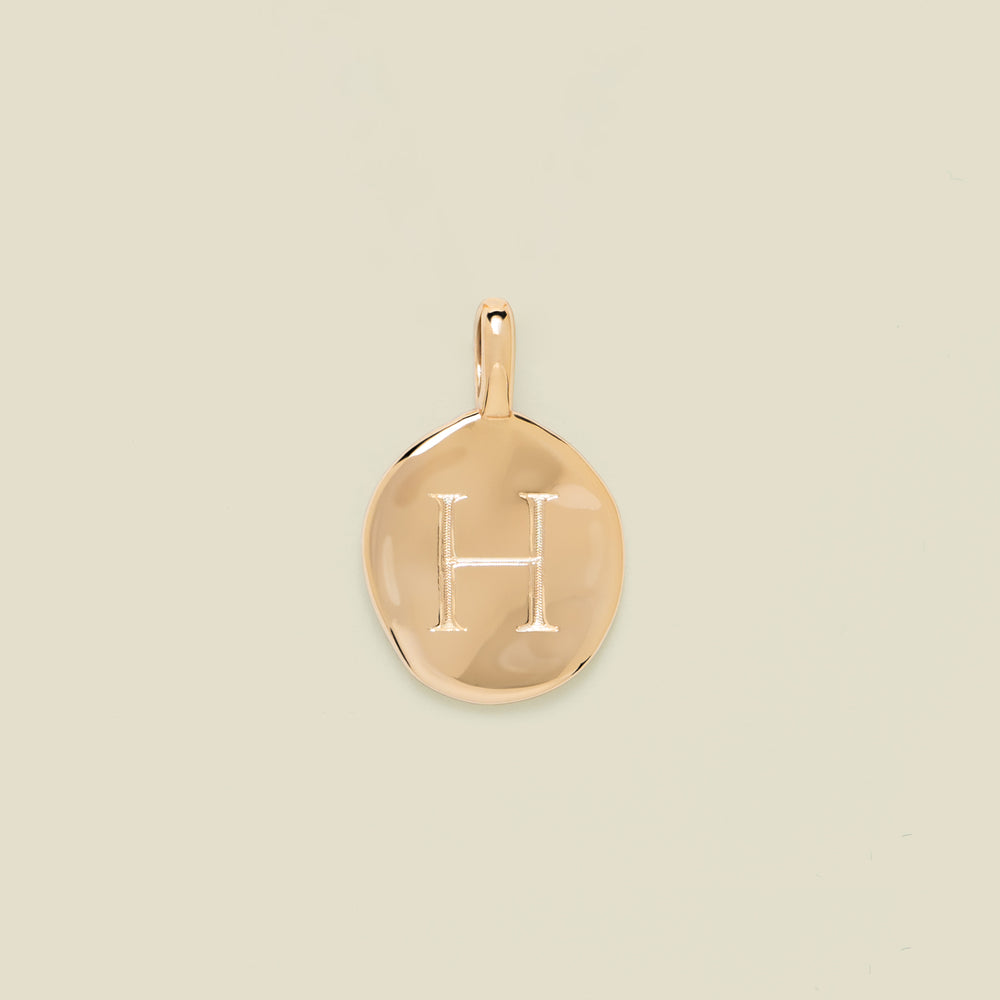 Gold pendant engraved with the letter 'H' on a beige background