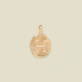 Gold pendant engraved with the letter 'H' on a beige background