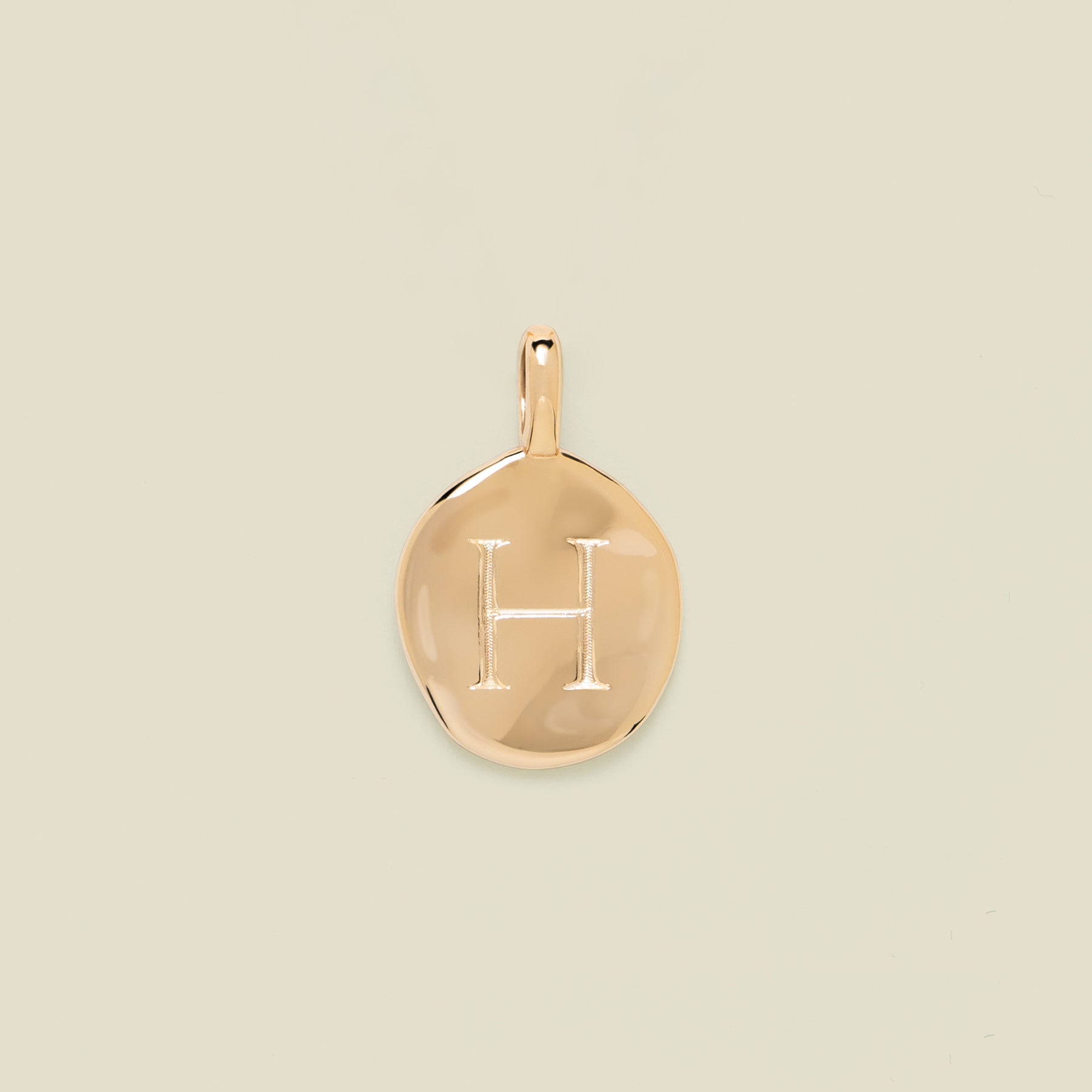 Gold pendant engraved with the letter 'H' on a beige background