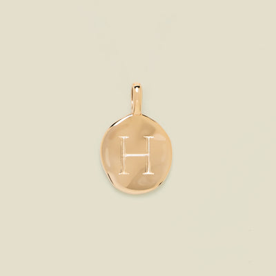Gold pendant engraved with the letter 'H' on a beige background