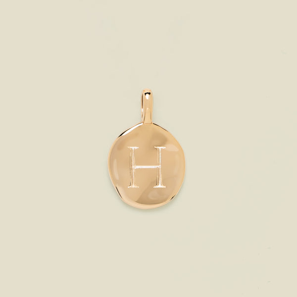 Gold pendant engraved with the letter 'H' on a beige background