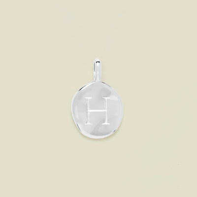 Silver pendant engraved with letter 'H' on a beige background