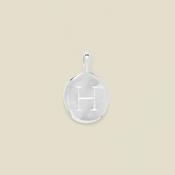 Silver pendant engraved with letter 'H' on a beige background