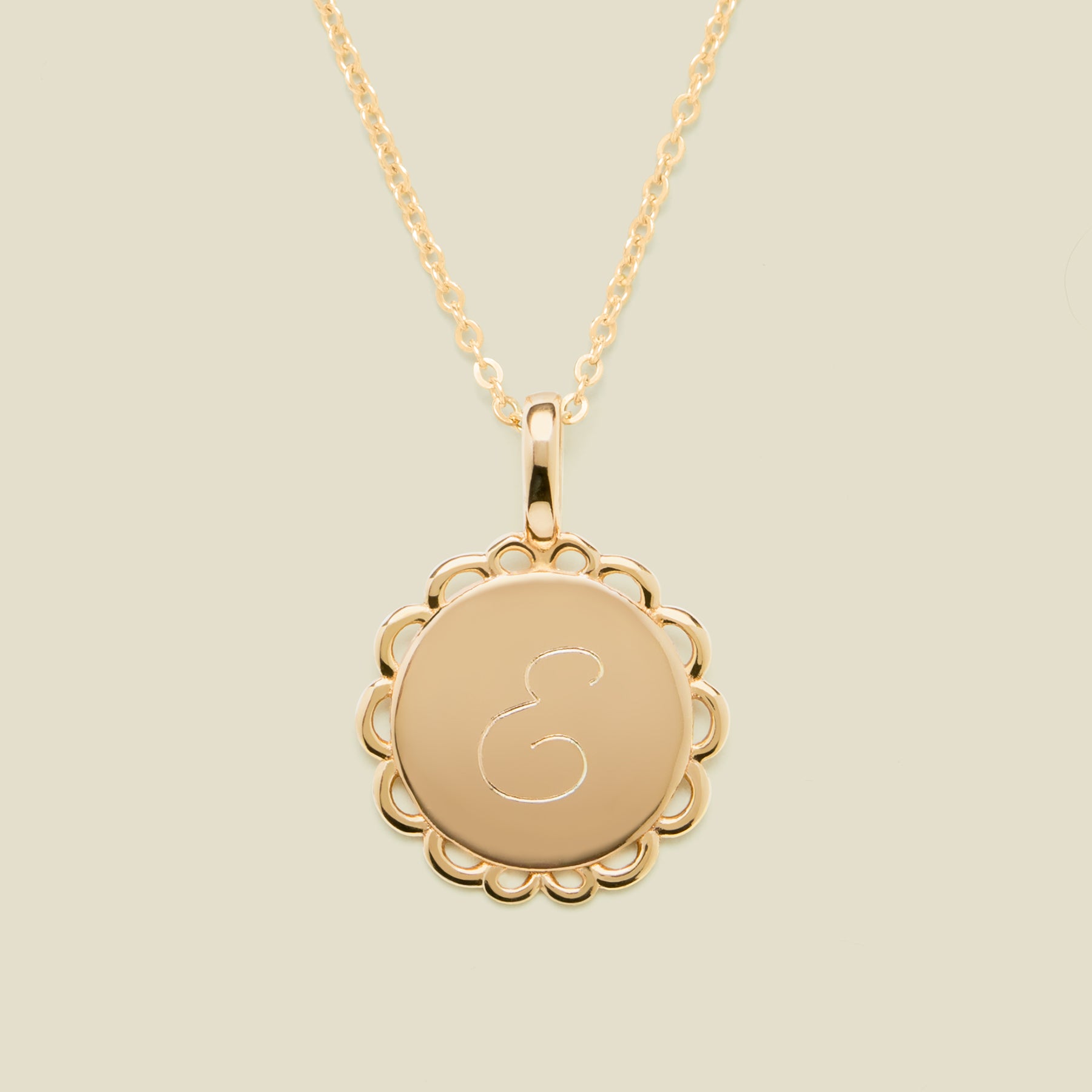 Gold necklace with a round pendant engraved with the letter "E" on a beige background
