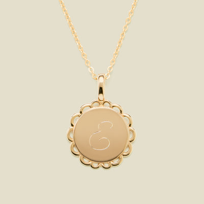 Gold necklace with a round pendant engraved with the letter "E" on a beige background