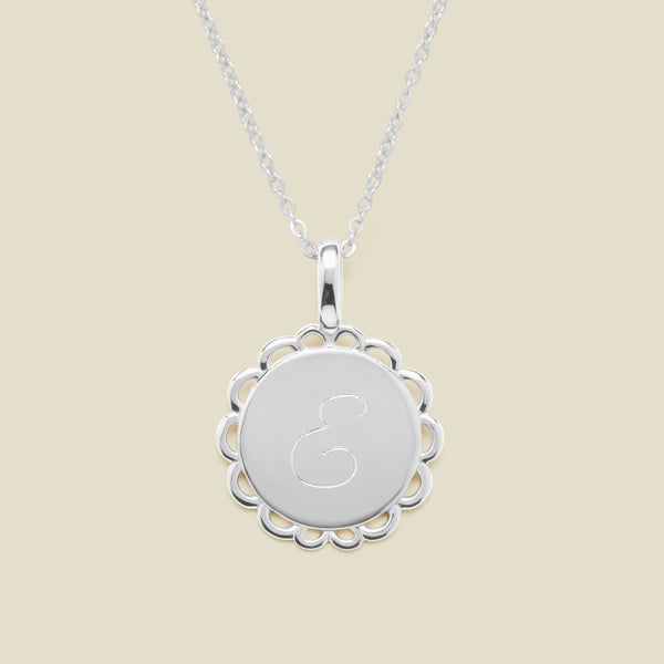 Silver necklace with a round pendant engraved with the letter "E" on a beige background