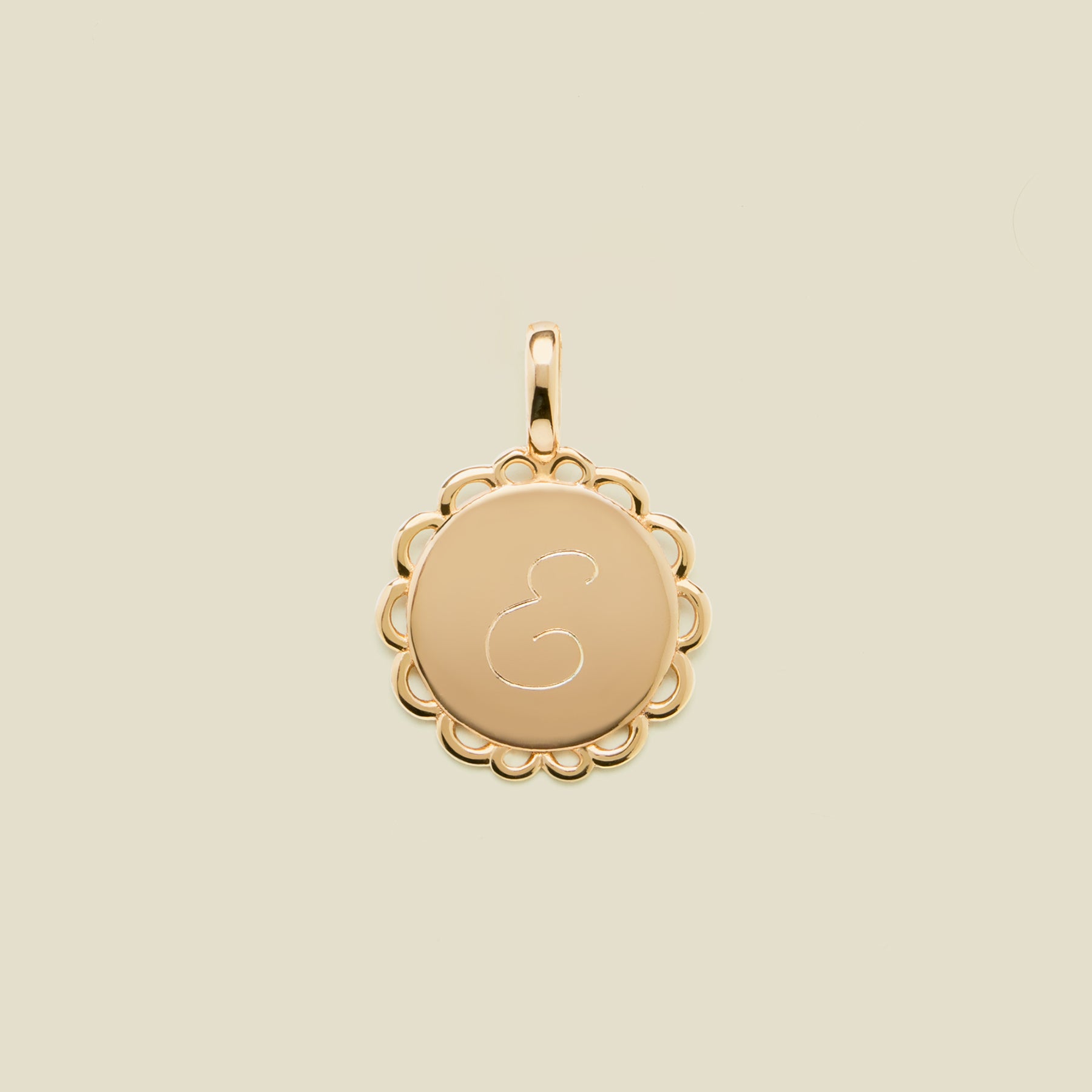 Gold pendant with engraved letter 'E' on a beige background